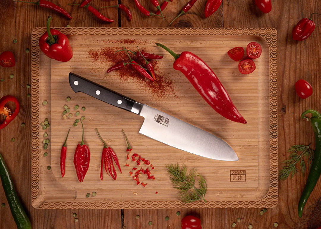 KOTAI Hashi Santoku met 17 cm lemmet op snijplank naast rode pepers